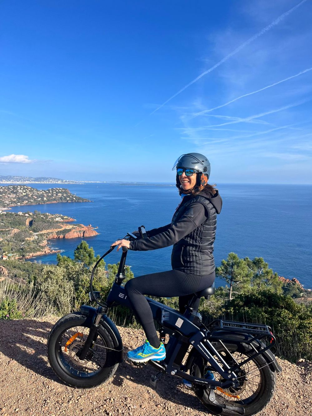 Una donna con casco seduta su una e-bike affacciata sul mare.