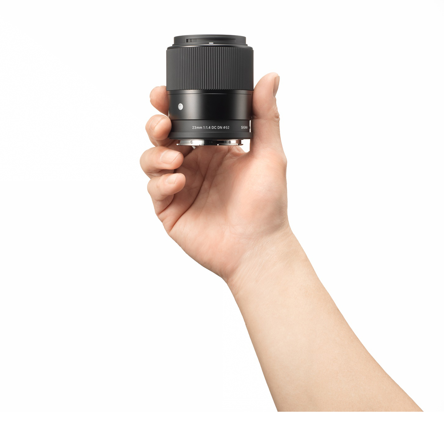 Una mano tiene un obiettivo fotografico nero con la scritta 23mm 1:1.4 DC DN.