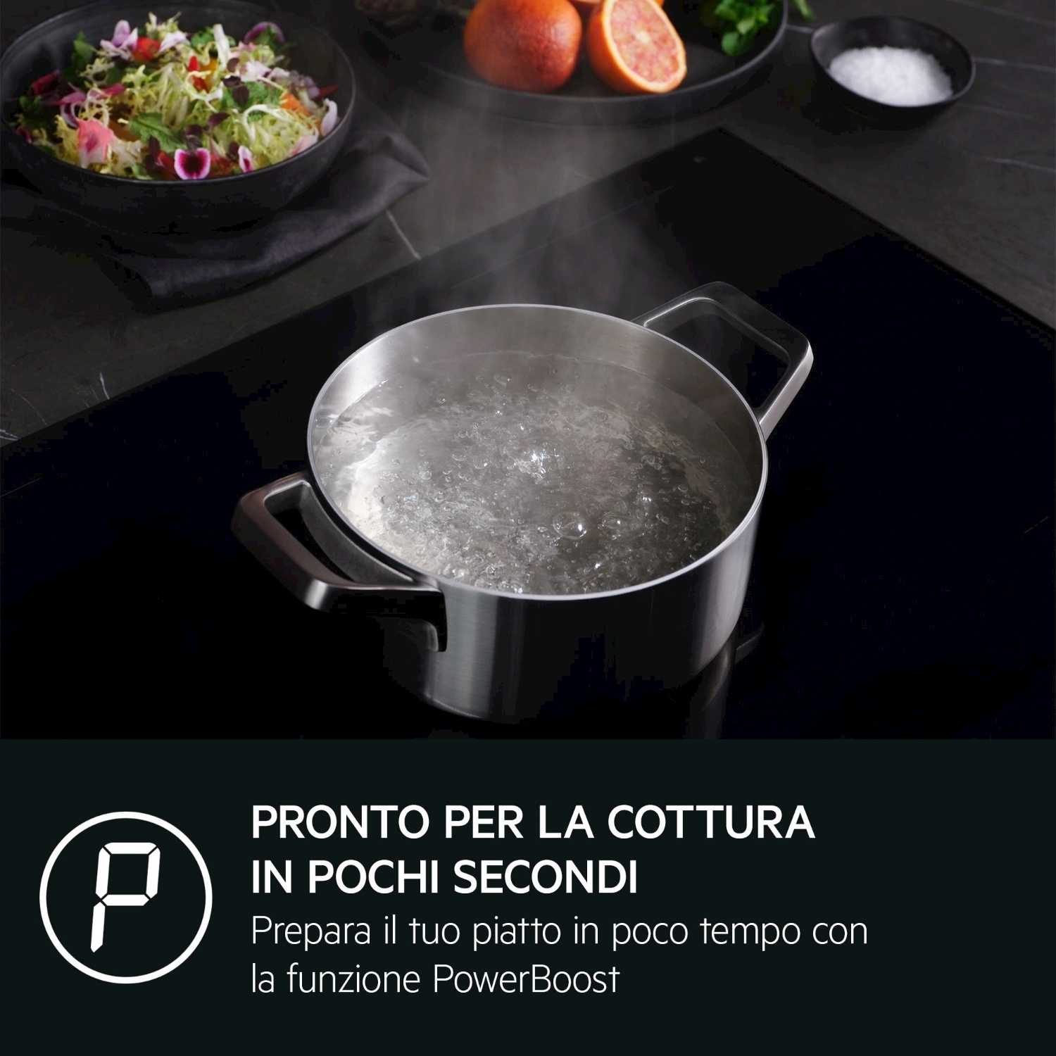 Una pentola di acqua bollente su un piano cottura a induzione, accanto a un'insalata.