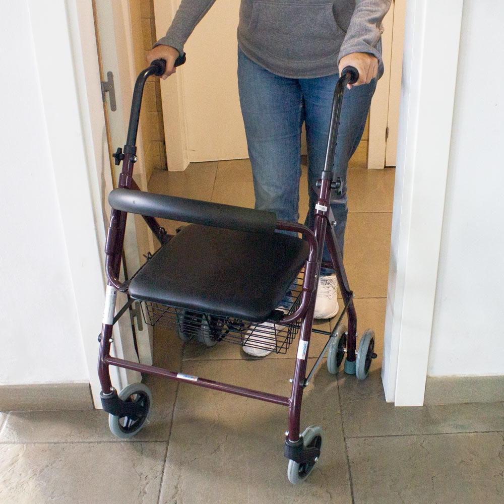 Persona usa un andador con asiento y cesta para pasar por una puerta.