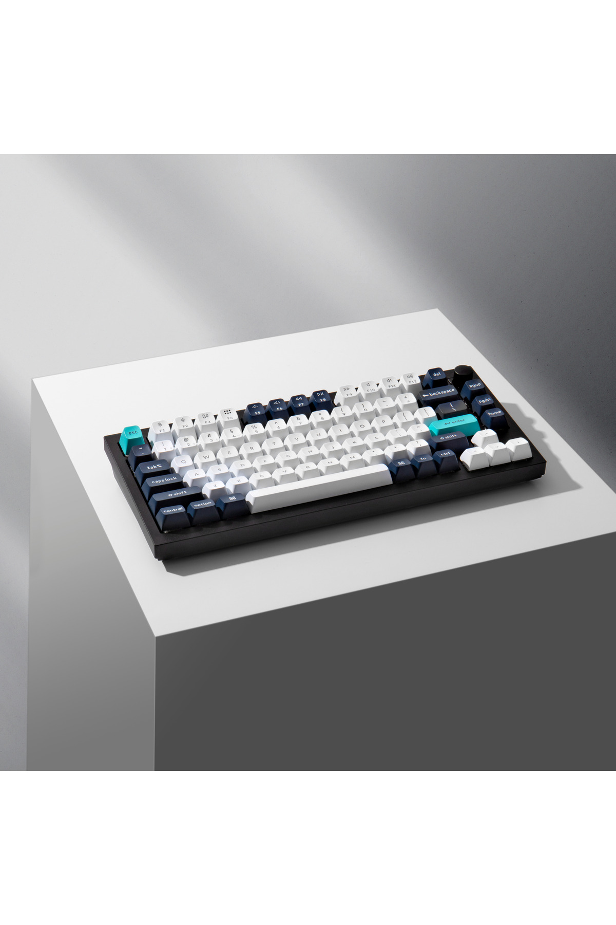 Un teclado mecánico negro con teclas blancas, azules y turquesas sobre una superficie blanca.