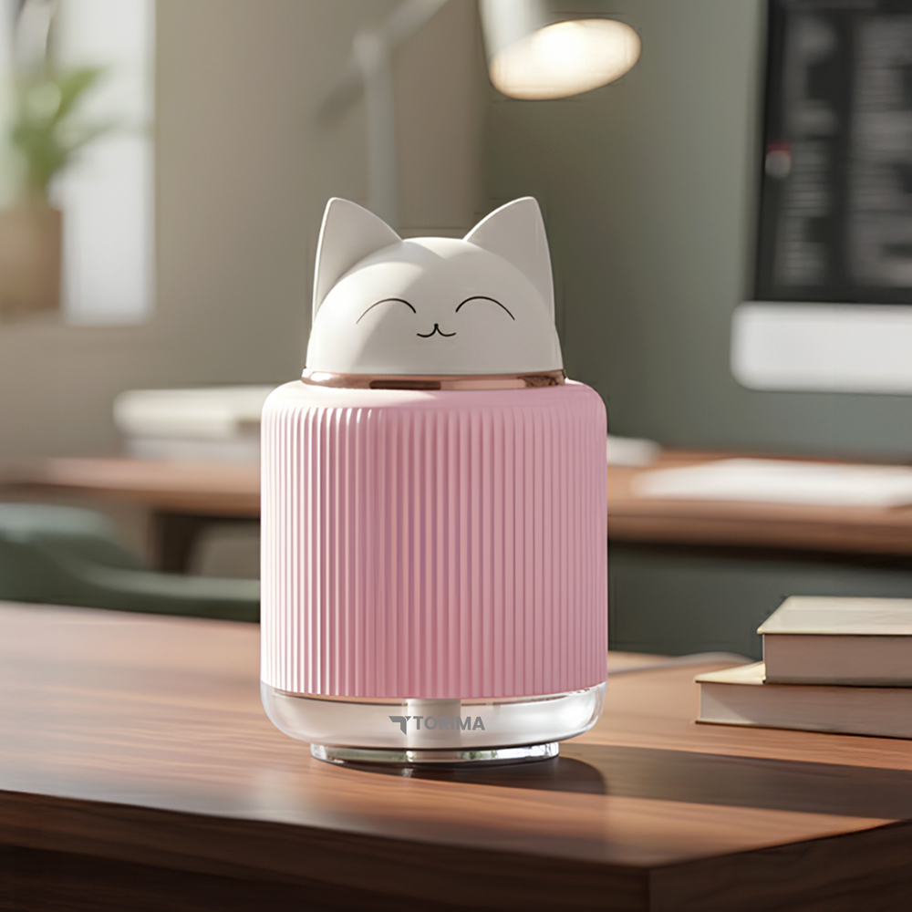 Üstünde beyaz kedi başı olan pembe bir difüzör ahşap bir masanın üzerinde duruyor.