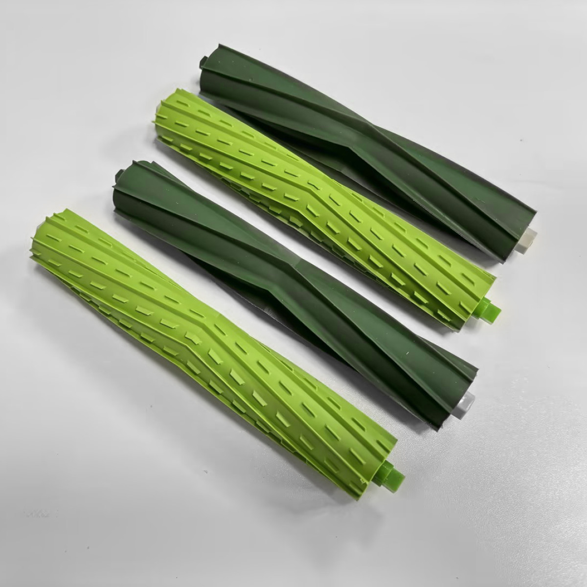 Cztery zielone i ciemnozielone gumowe wałki do odkurzaczy leżą na białej powierzchni.