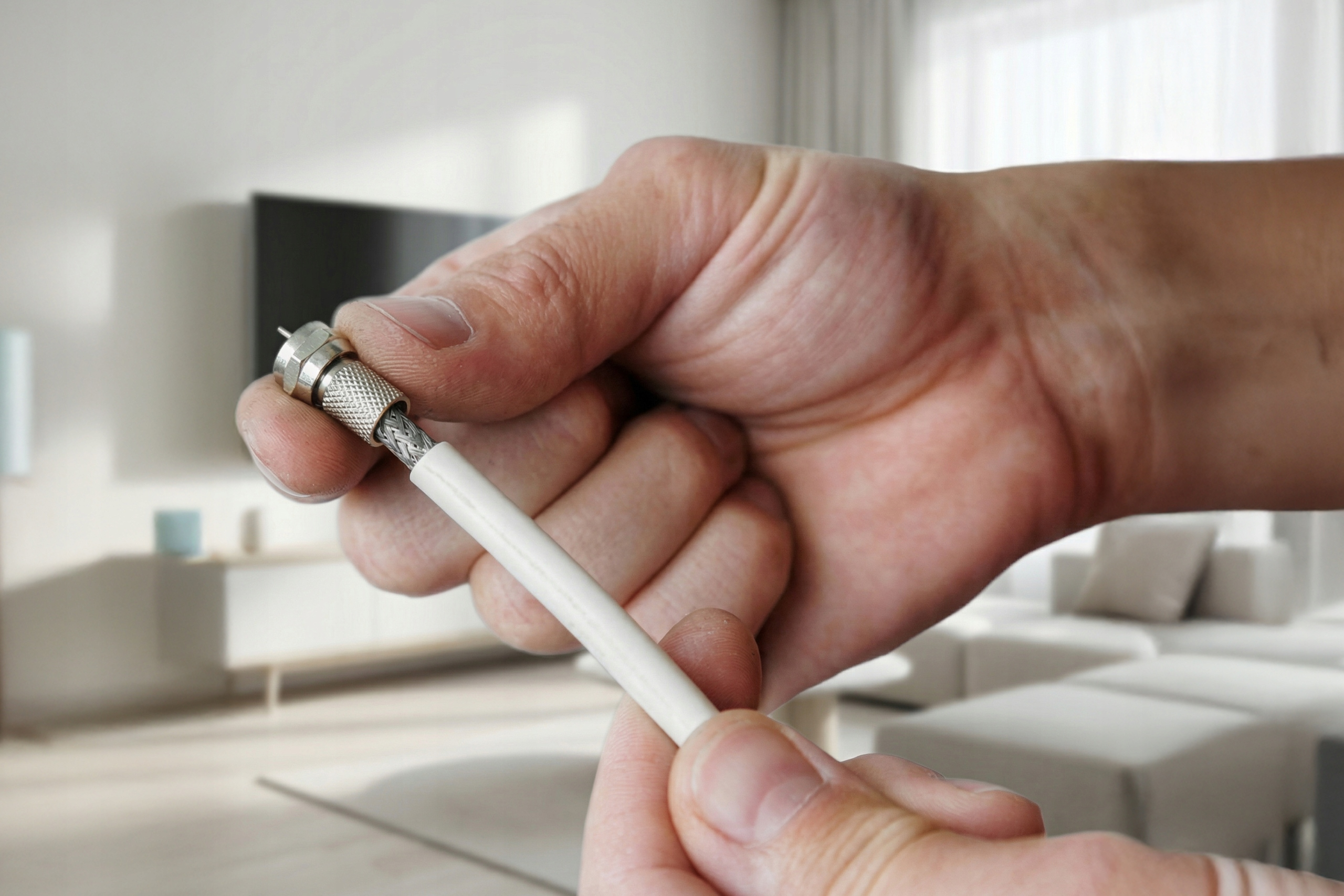 Zbliżenie dłoni trzymającej biały kabel ze srebrną wtyczką. Rozmyte tło.