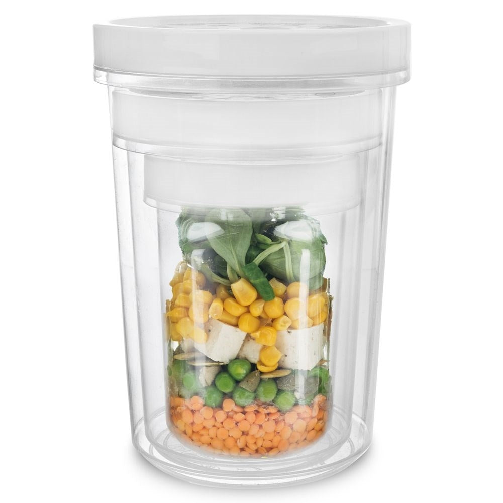 Un recipiente transparente con capas de comida: lentejas, guisantes, maíz, tofu y verduras.