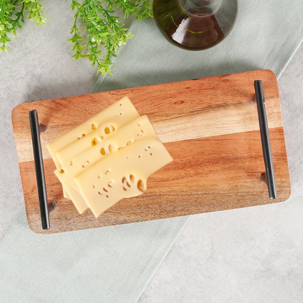 Queso en lonchas apilado sobre tabla de madera con asas, junto a ramitas verdes y botella.