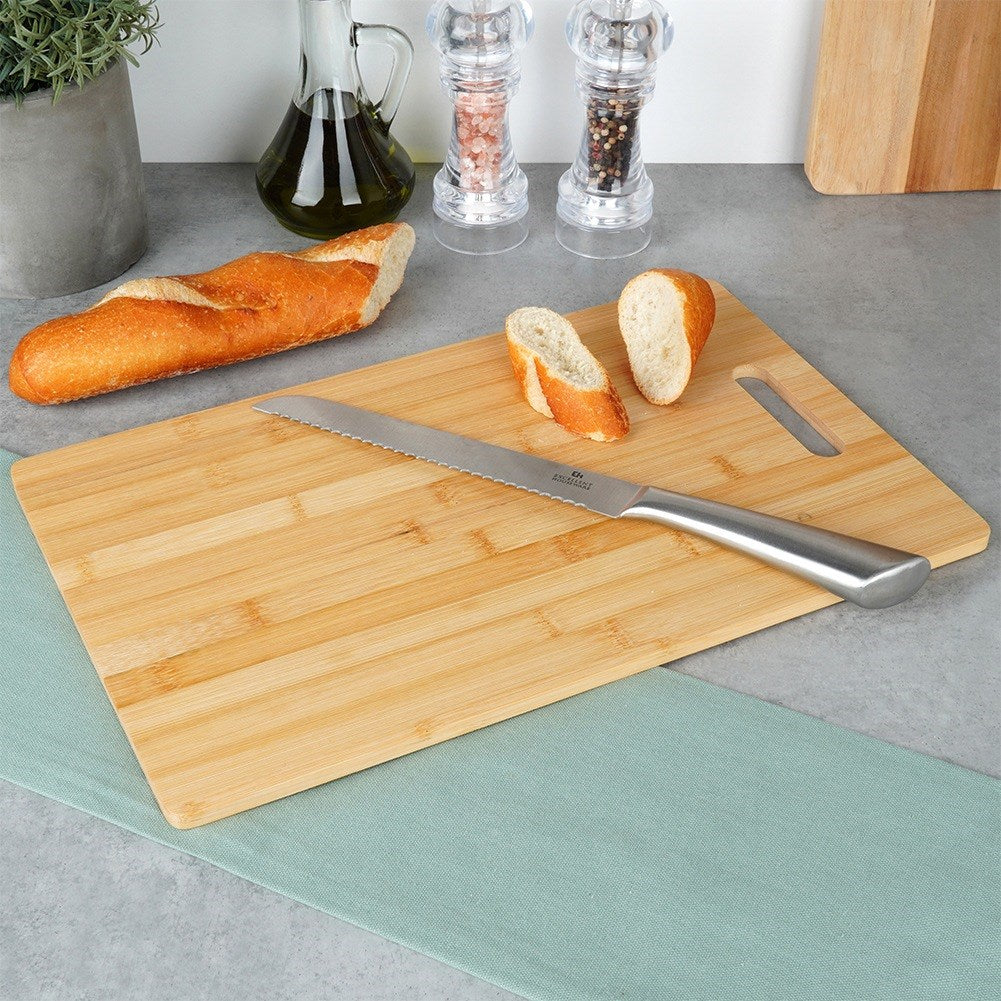 Un cuchillo para pan yace sobre una tabla de cortar de madera junto a una baguette y dos rebanadas.