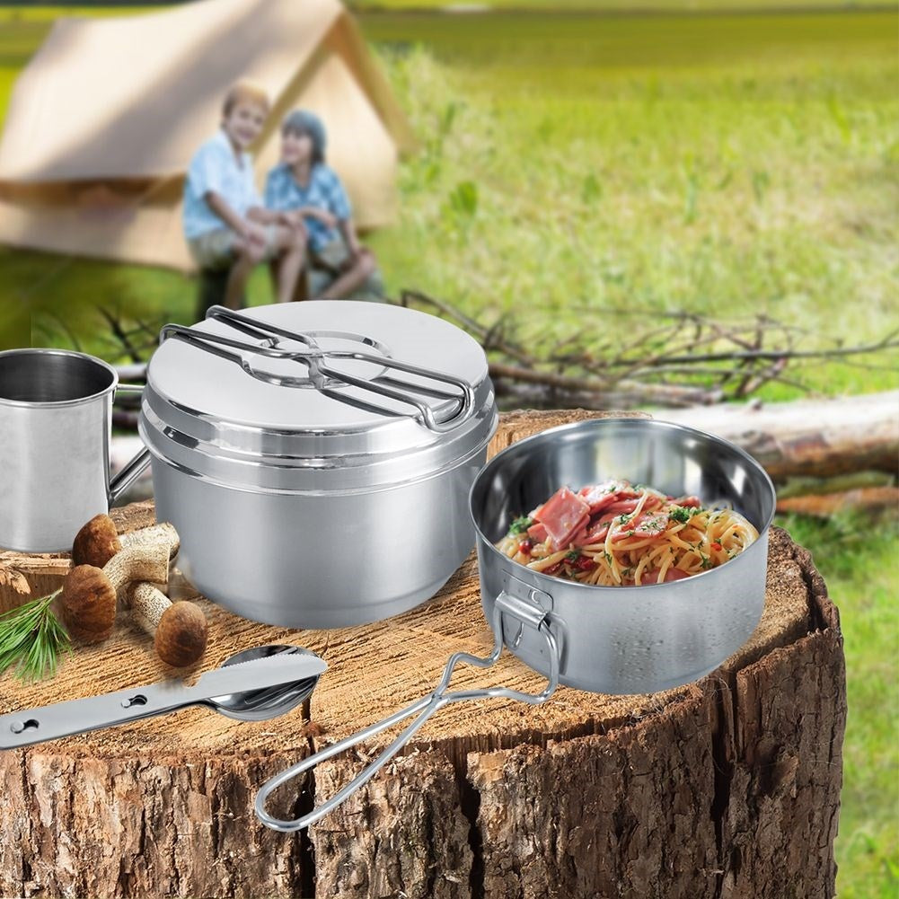 Utensilios de camping en tocón: olla, cuenco con pasta, taza, champiñones, cuchara.