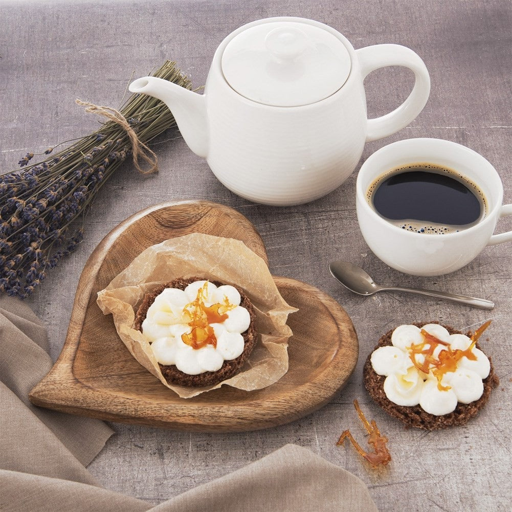 Una tetera blanca, una taza de café y dos galletas con crema y caramelo.