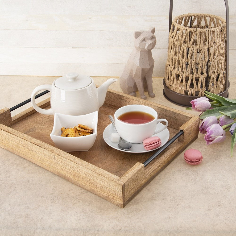 Una bandeja de madera con tetera, taza, galletas, macarons y decoraciones.