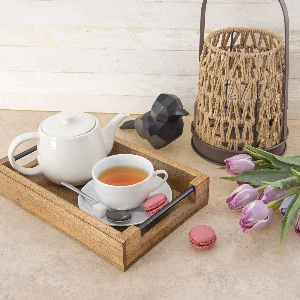 Una tetera, taza, macarons y decoración de pájaro en una bandeja.