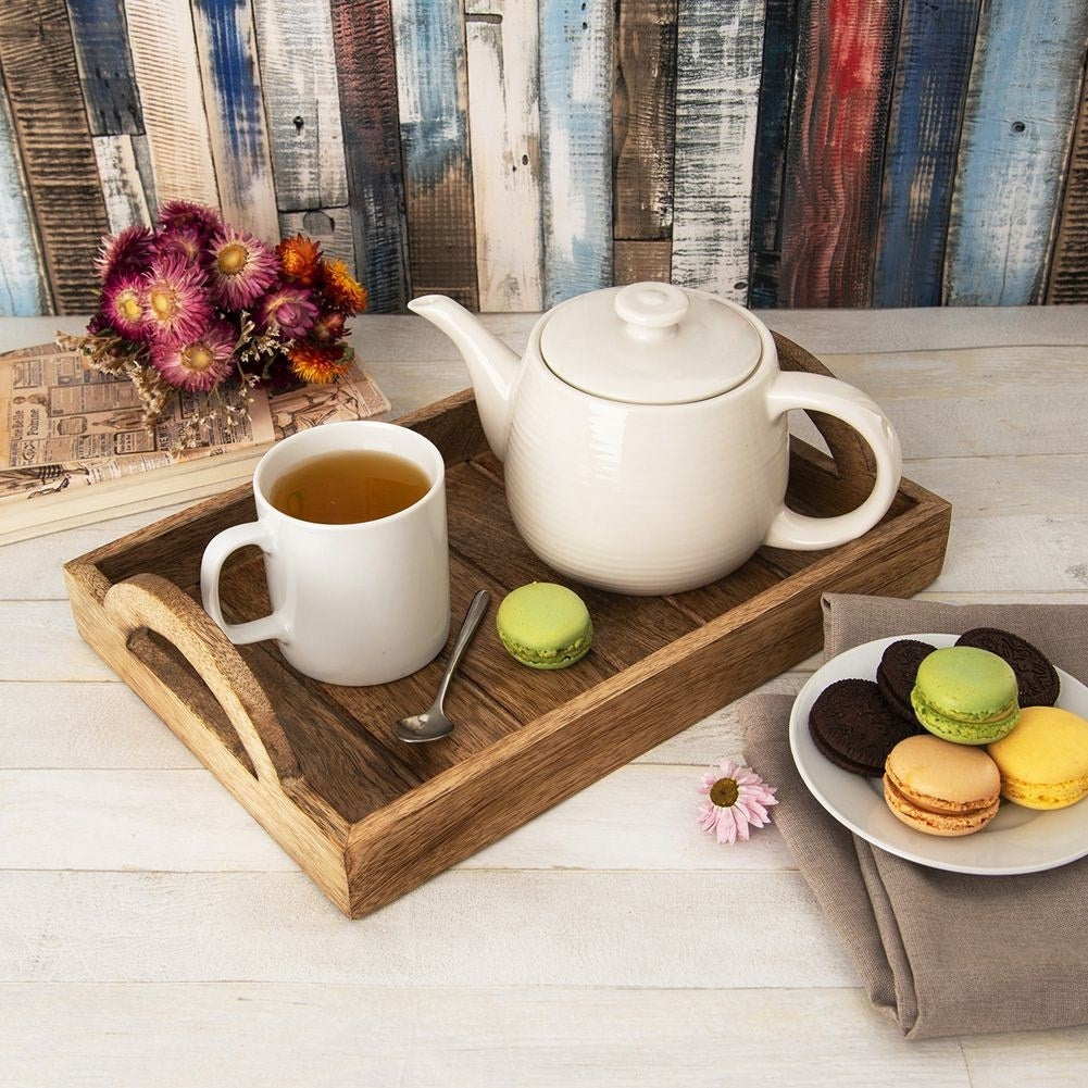 Bandeja de madera con tetera, taza, flores y galletas sobre fondo de madera.