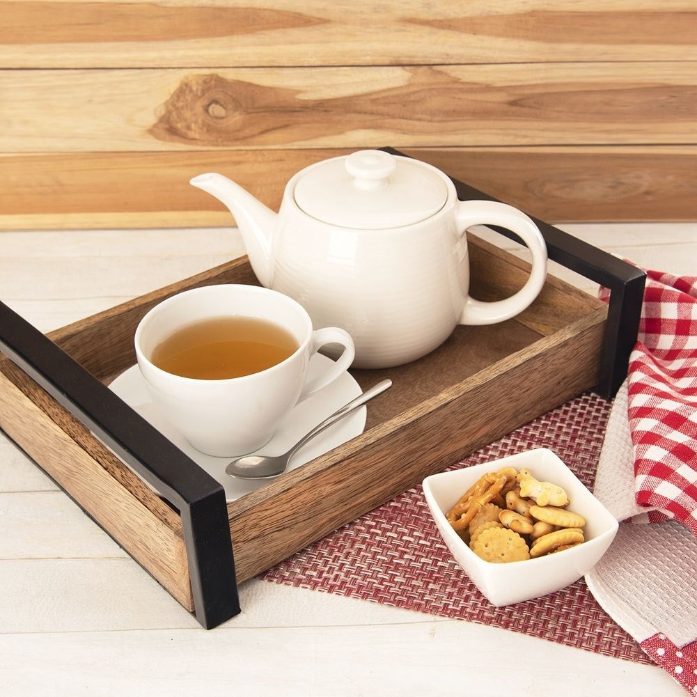 Una bandeja de madera con tetera, taza de té, cuchara y galletas.