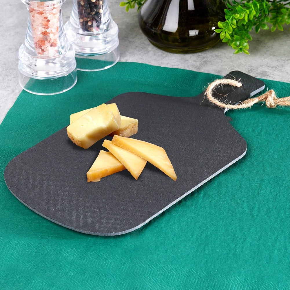 Cubos de queso sobre tabla oscura con asa de cuerda, saleros y pimenteros cerca.
