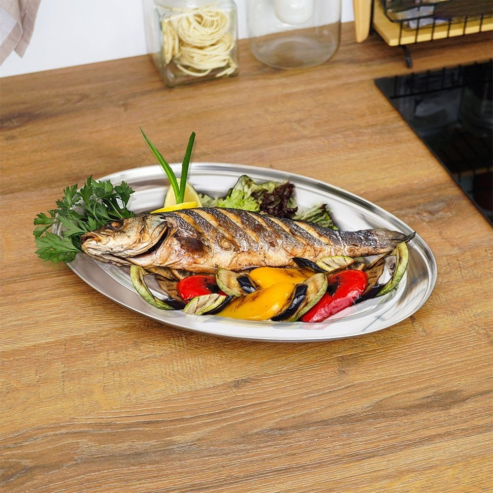 Pescado a la parrilla con tiras de verduras coloridas en una bandeja de plata ovalada.