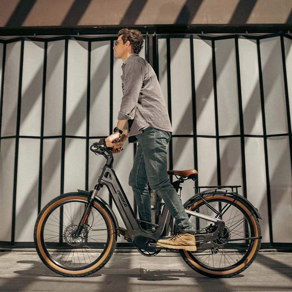 Un hombre monta una bicicleta eléctrica oscura frente a una pared plegada con sombras.
