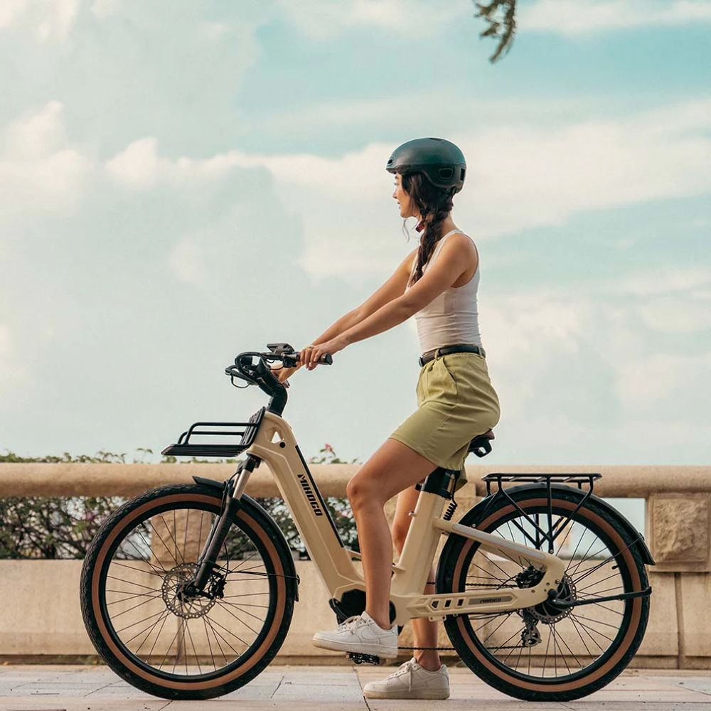Una mujer con casco monta una bicicleta beige bajo un cielo nublado.