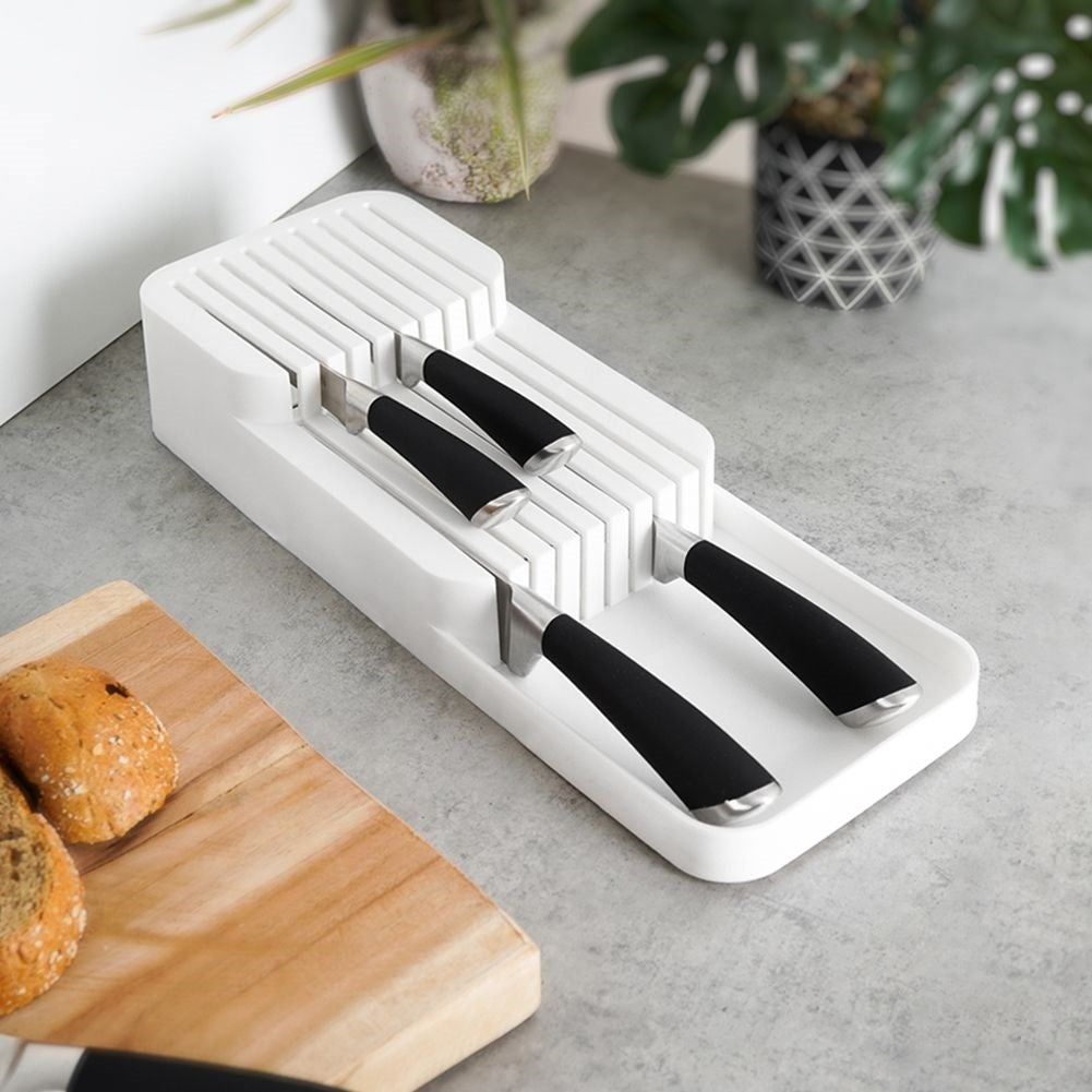 Un ceppo portacoltelli bianco con coltelli manico nero su un piano di lavoro.