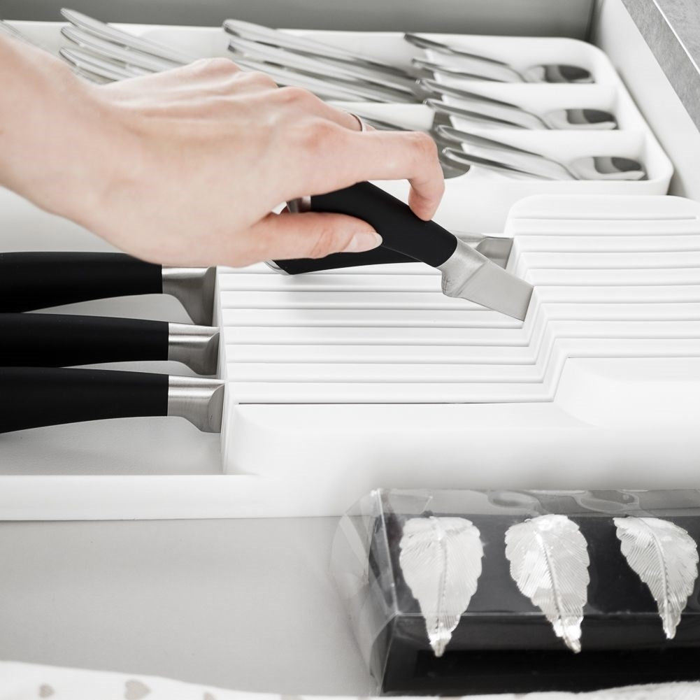 Una mano posiziona un coltello con manico nero in un ceppo portacoltelli bianco.
