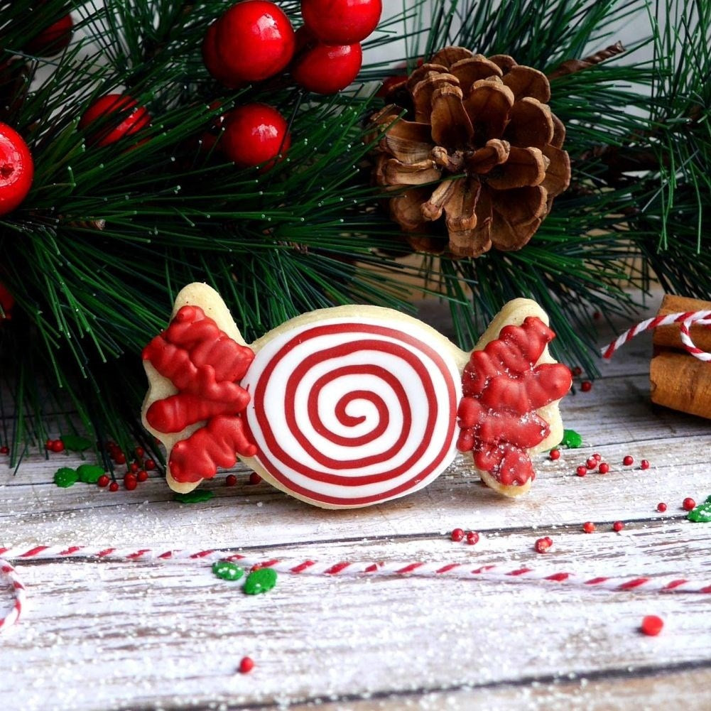Una galleta navideña con forma de caramelo, espirales rojas y blancas y glaseado rojo.