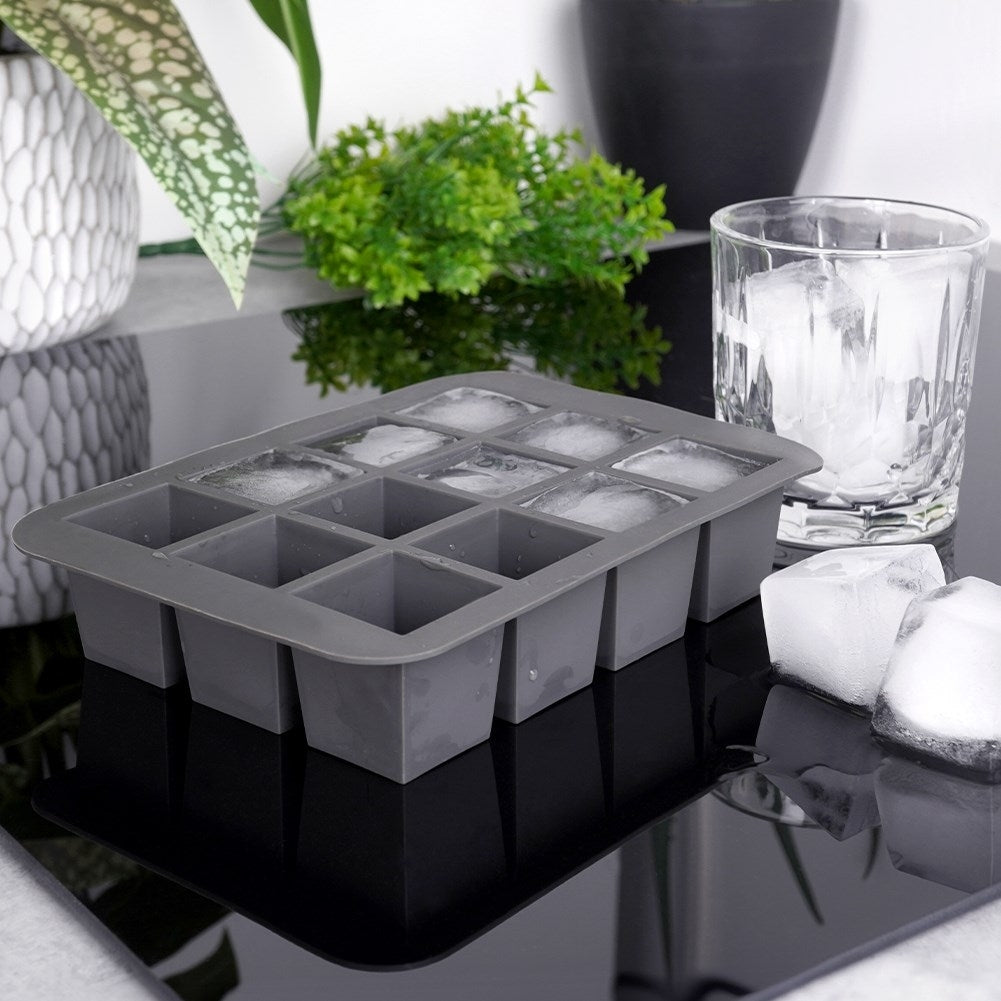 Molde gris para cubitos de hielo con cubitos, vaso y cubitos sueltos cerca.