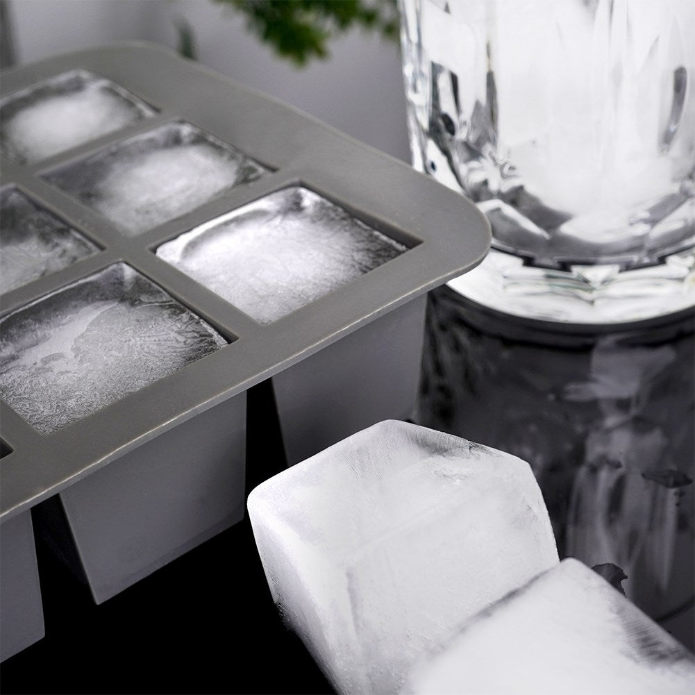 Cubilera gris con cubos congelados, al lado un vaso con hielo.