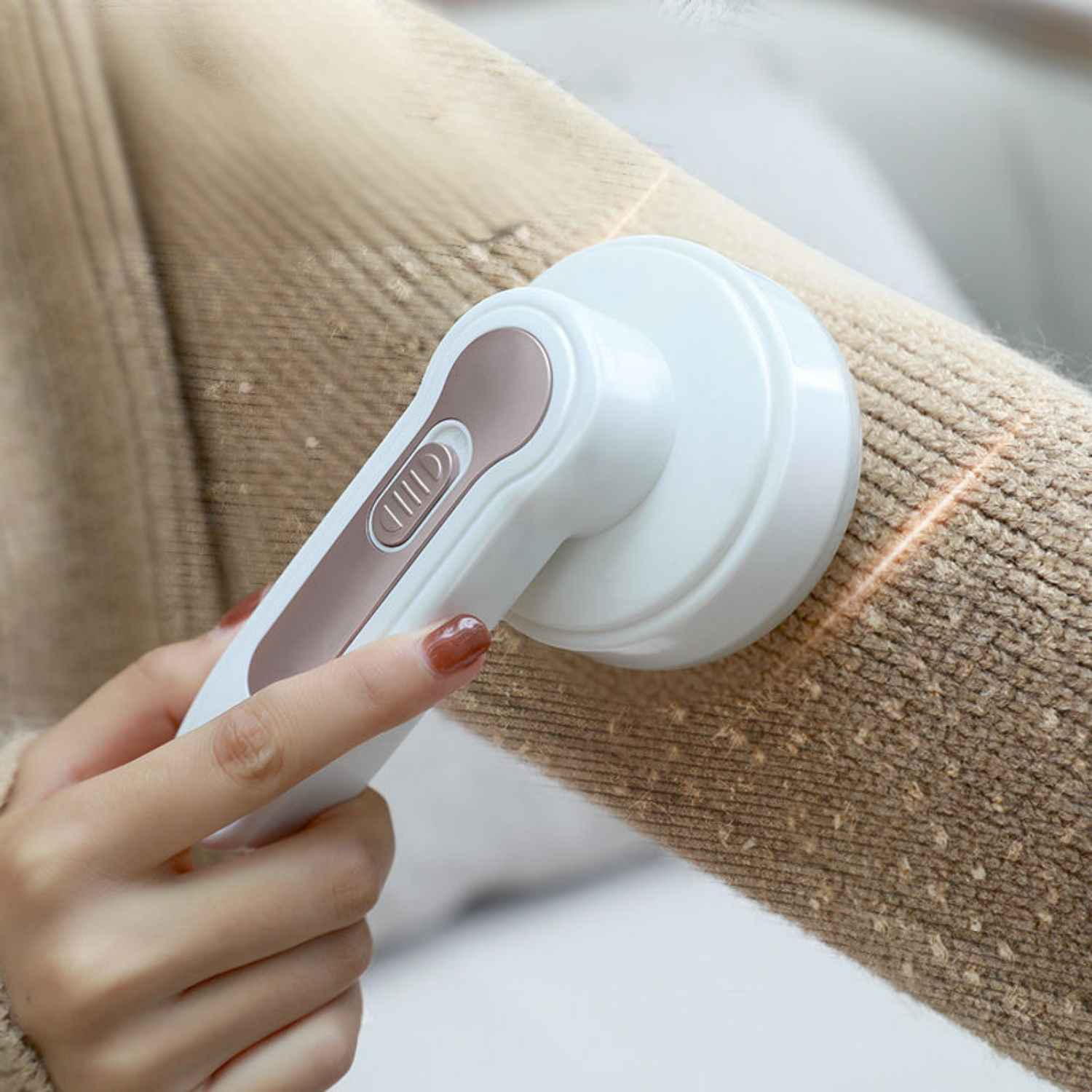Eine Hand hält einen Fusselentferner über einem beigen Pullover, der Fussel entfernt.