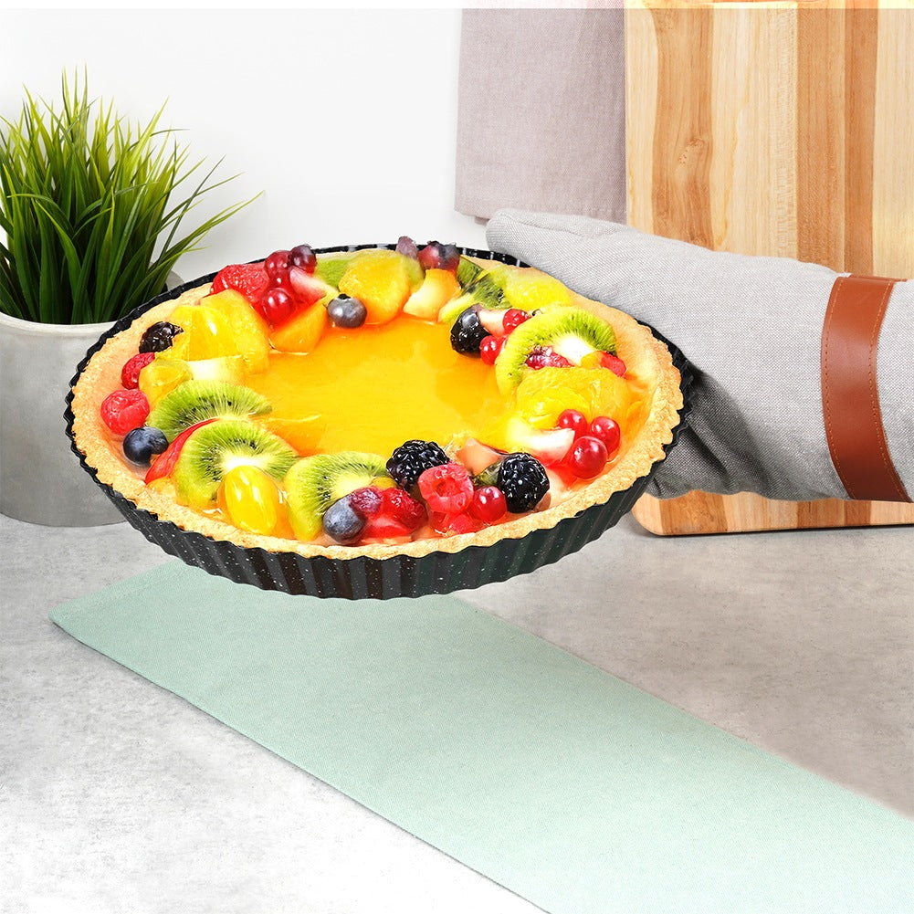 Tarta de frutas con bayas y kiwi en un molde negro sobre una encimera.