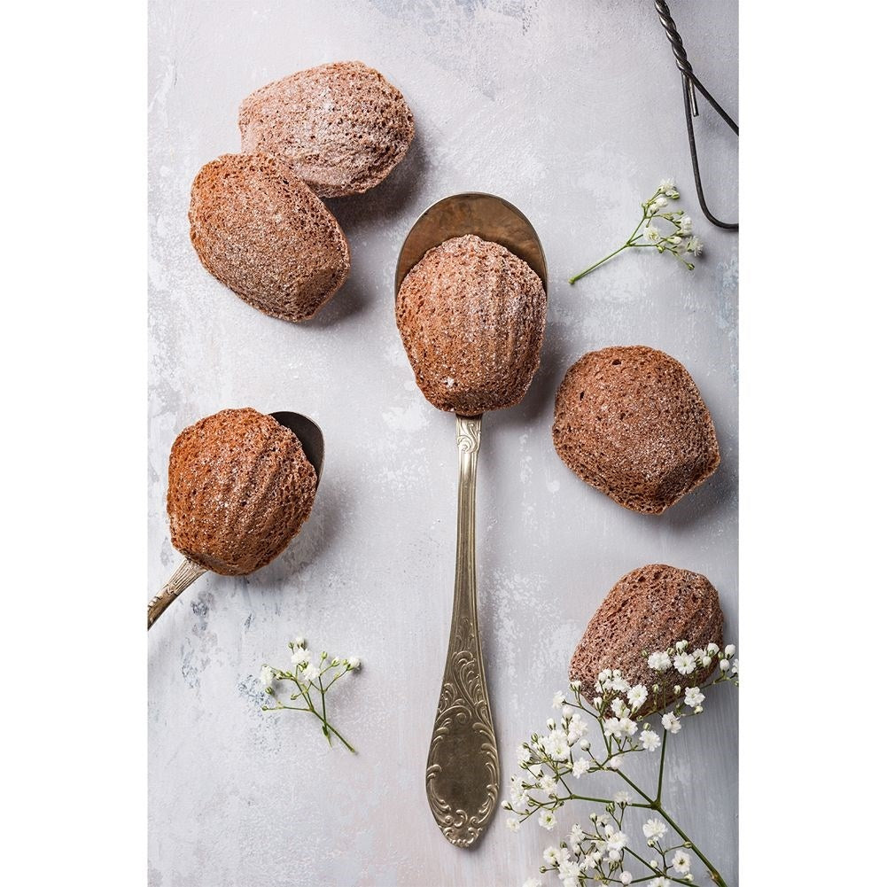 Madeleines de chocolate en cucharas y superficie, con flores blancas.