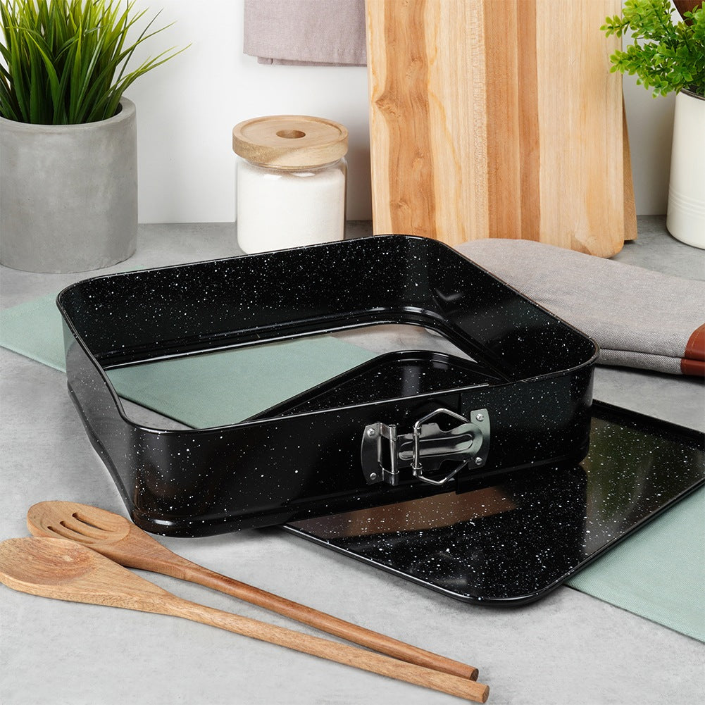 Un molde cuadrado negro moteado para tarta con base extraíble y dos cucharas de madera.