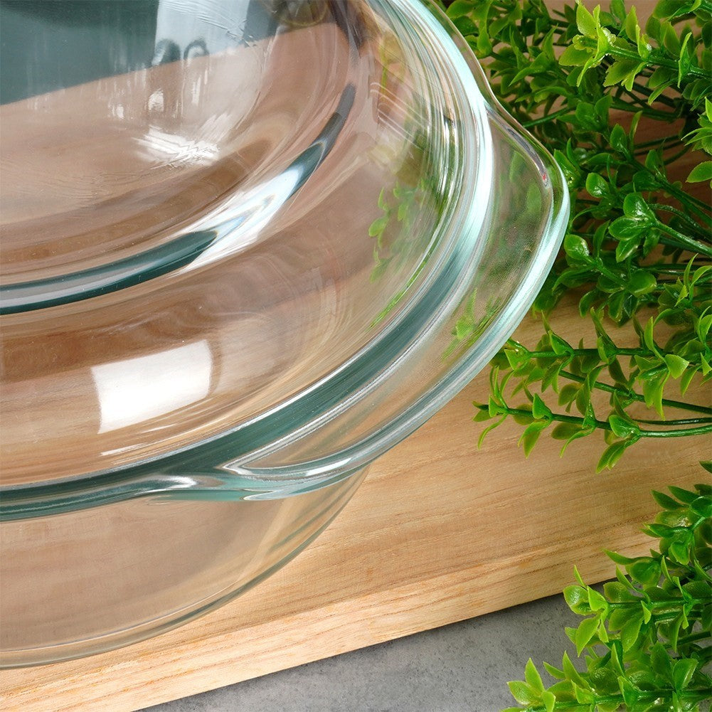 Un cuenco de vidrio transparente con asas descansa sobre una tabla de madera junto a plantas verdes.