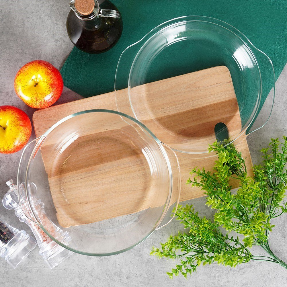 Dos moldes de tarta de cristal sobre tabla de madera con manzanas y aceite.