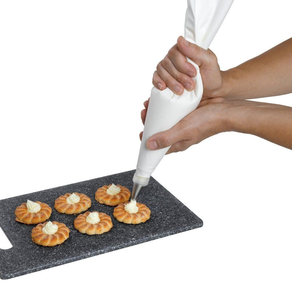 Manos decorando galletas con crema blanca sobre tabla.