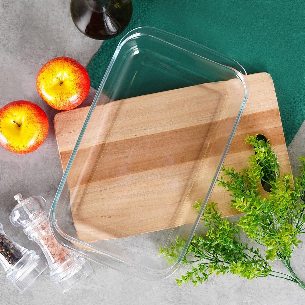 Fuente de vidrio sobre tabla de madera con manzanas, molinillos y decoración verde.
