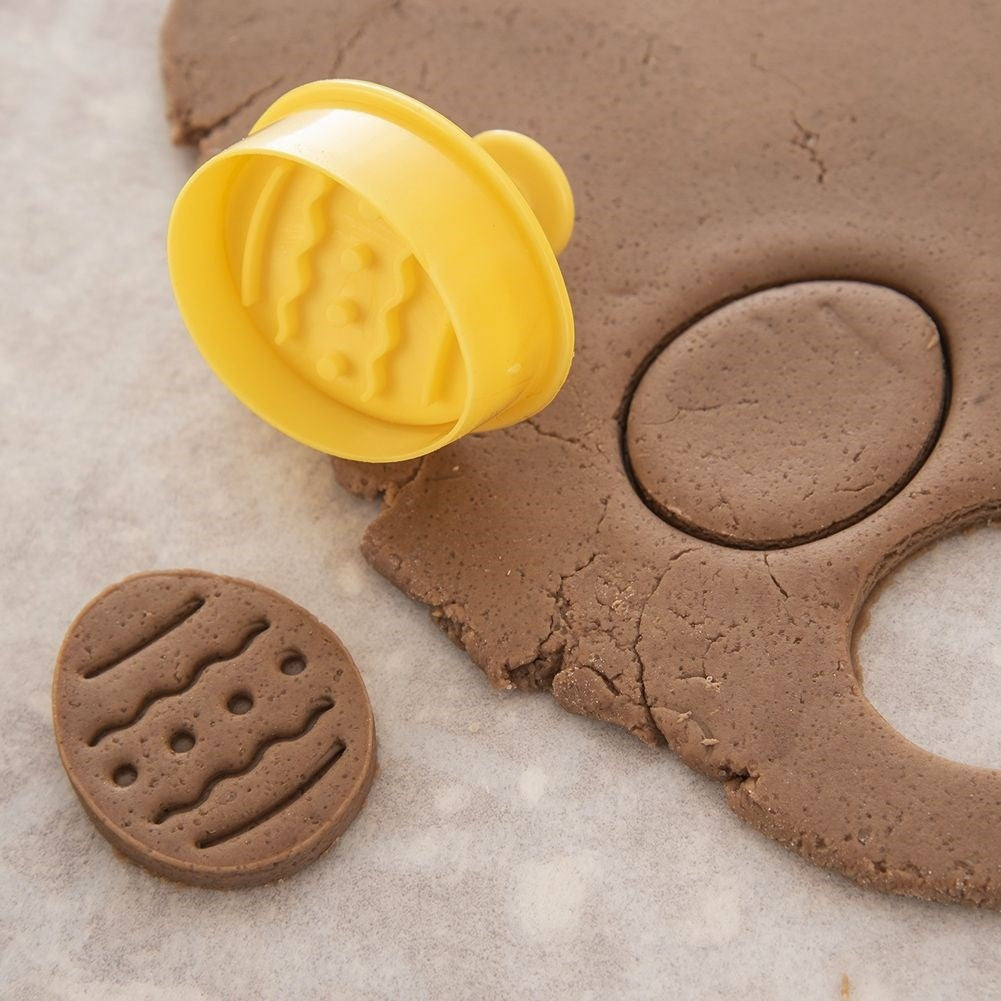 Un cortador de galletas amarillo descansa sobre masa marrón junto a una galleta.