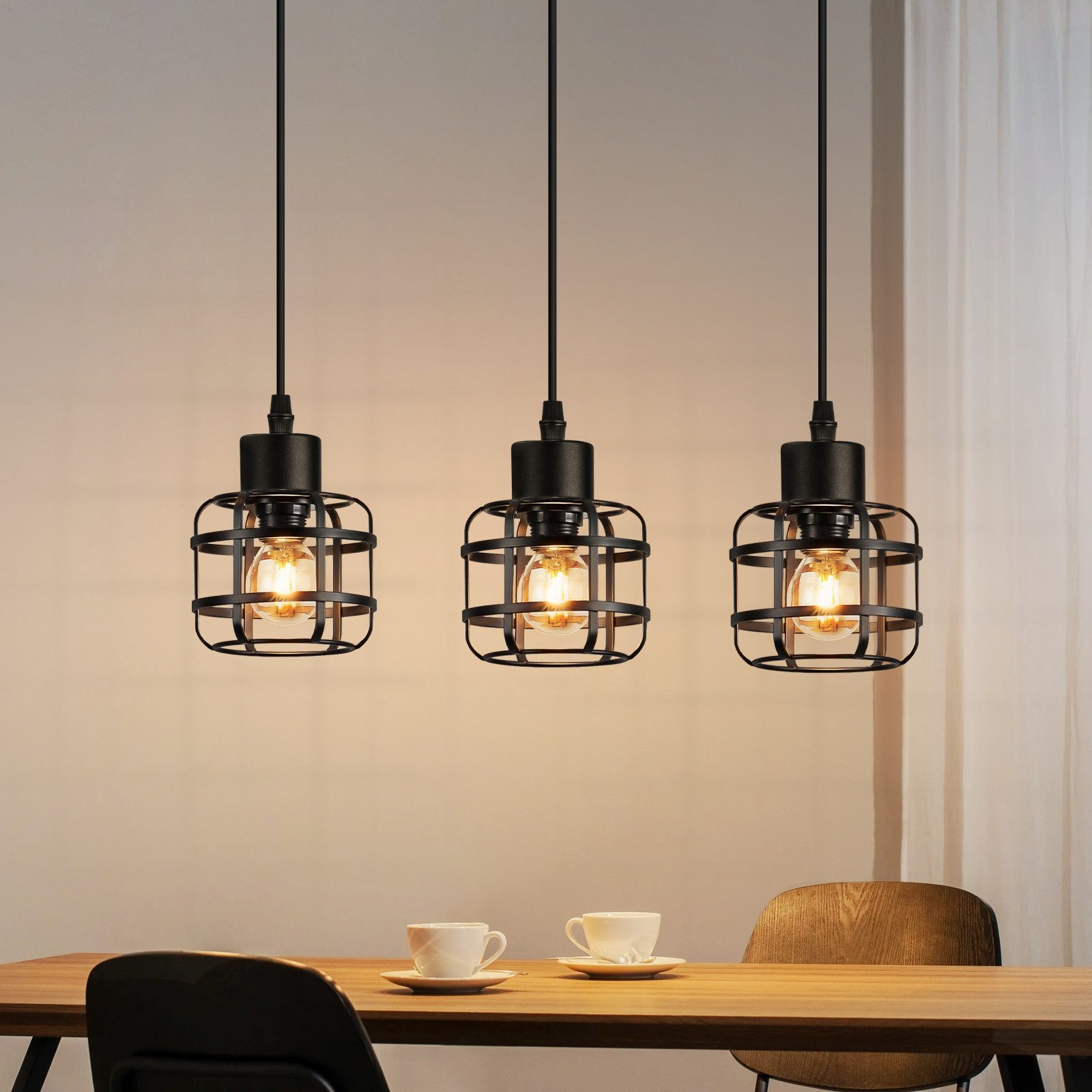 Drei schwarze Pendelleuchten mit Käfig-Design über einem Holztisch.