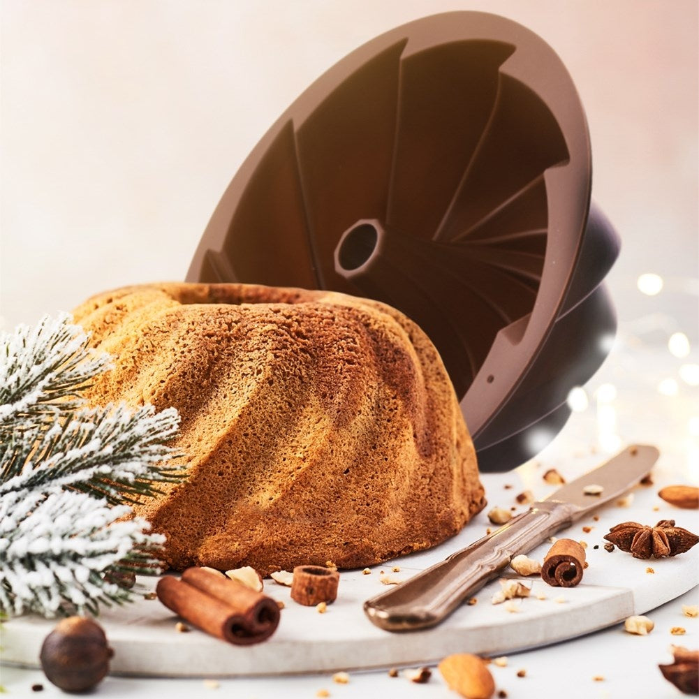 Un bizcocho tipo bundt junto a su molde con canela en una tabla.