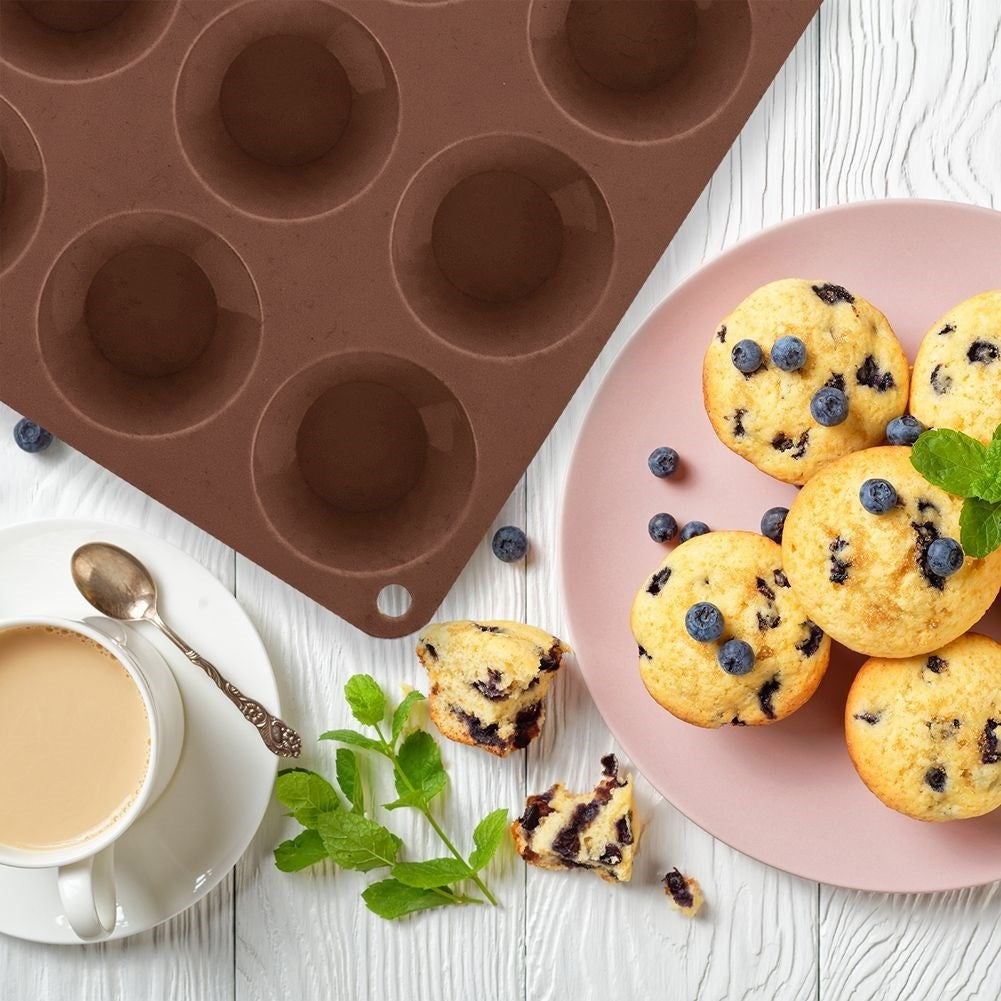 Molde para muffins marrón con muffins de arándanos, café y menta sobre fondo de madera.