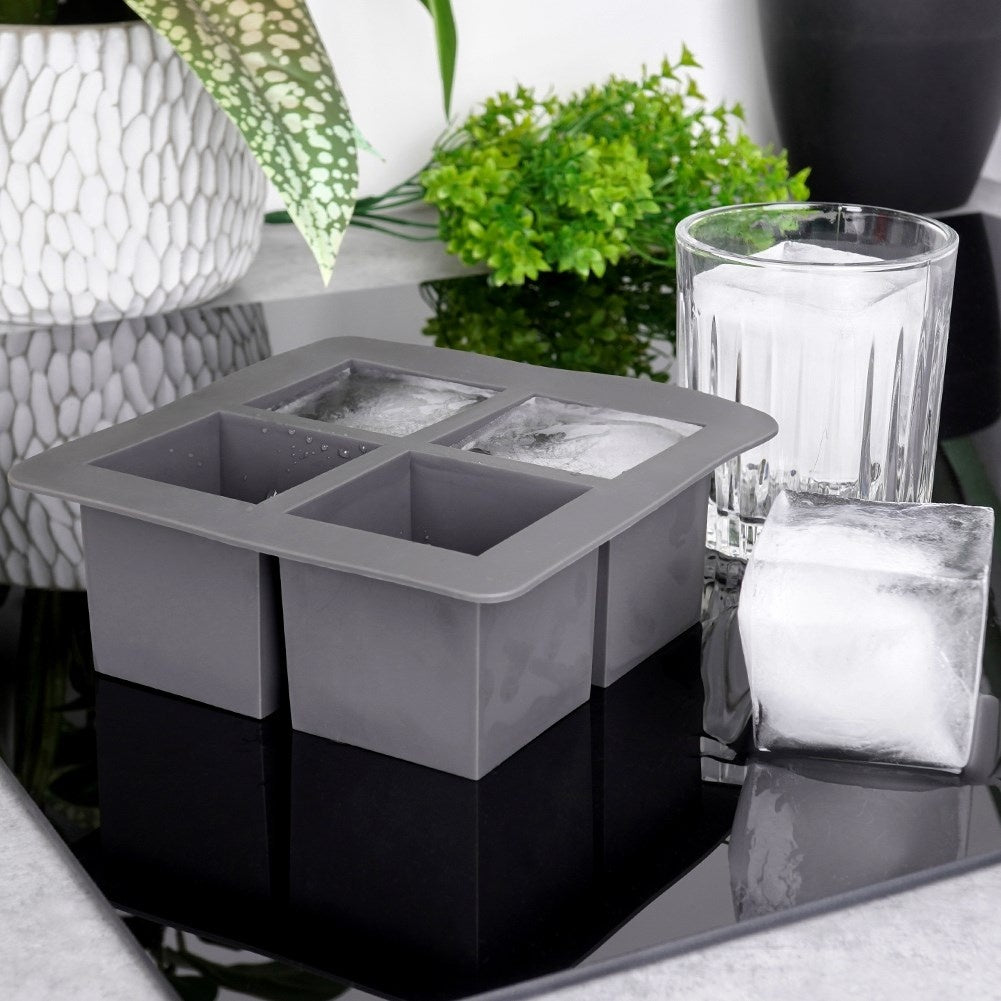 Molde de hielo gris con cuatro cubitos, vaso y un cubito al lado.