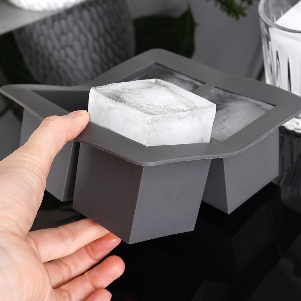 Una mano saca un gran cubito de hielo de una cubitera gris.