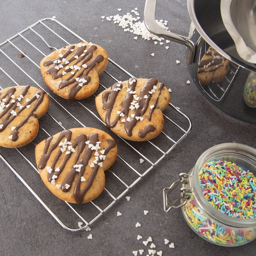 Galletas en forma de corazón con glaseado de chocolate y chispas en una rejilla.