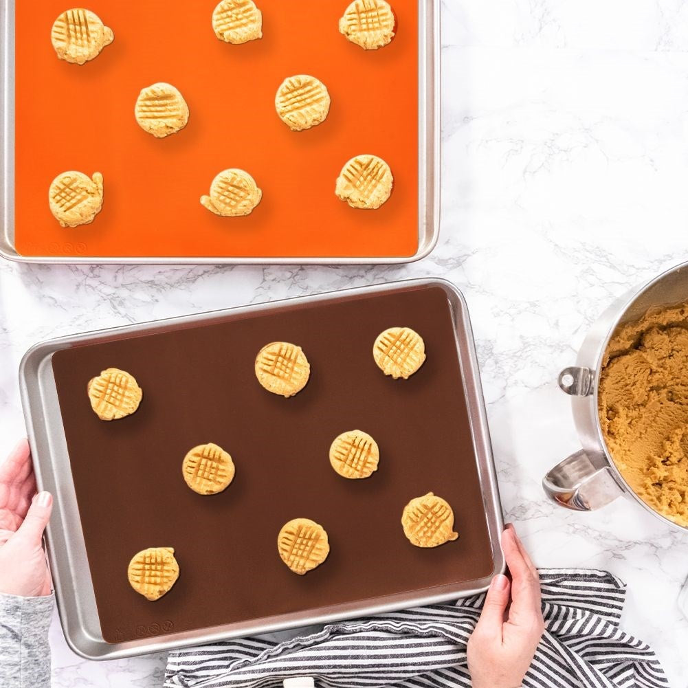 Galletas sin hornear en dos bandejas para hornear con tapetes de silicona marrones y naranjas.