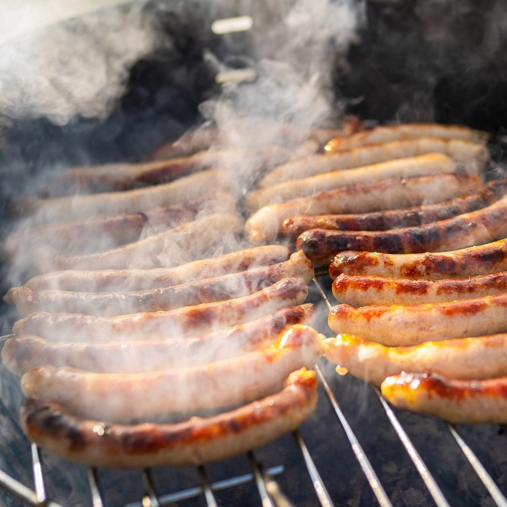 Muchas salchichas chisporrotean en una parrilla, rodeadas de vapor.