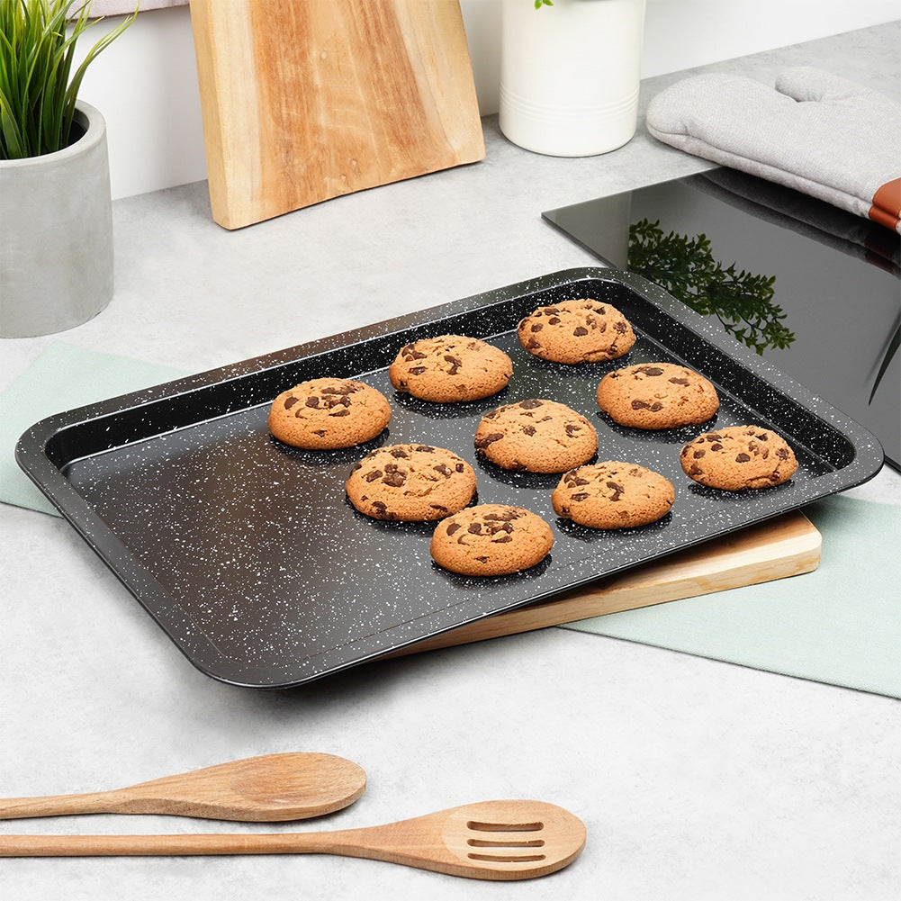 Una bandeja de horno tiene nueve galletas con chispas de chocolate. Dos cucharas de madera delante.