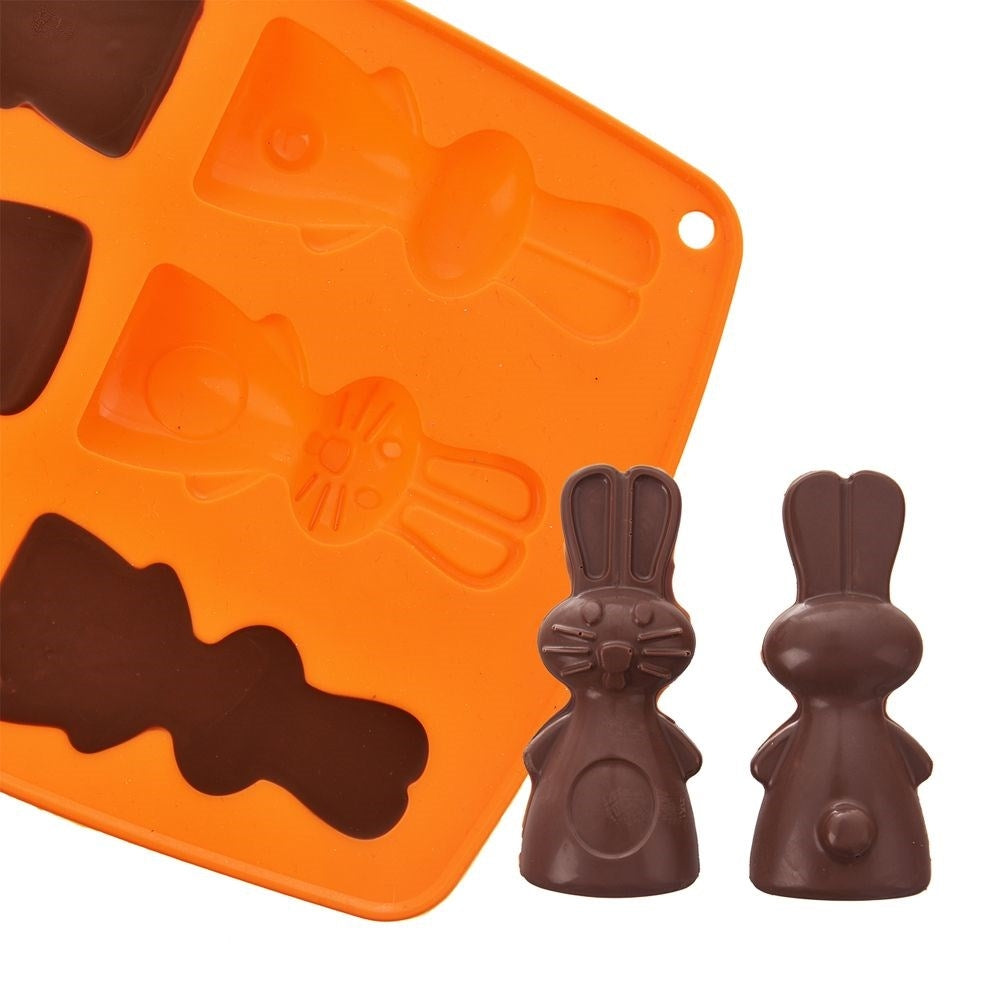 Un molde de silicona naranja con formas de conejito y dos conejitos de chocolate terminados al lado.