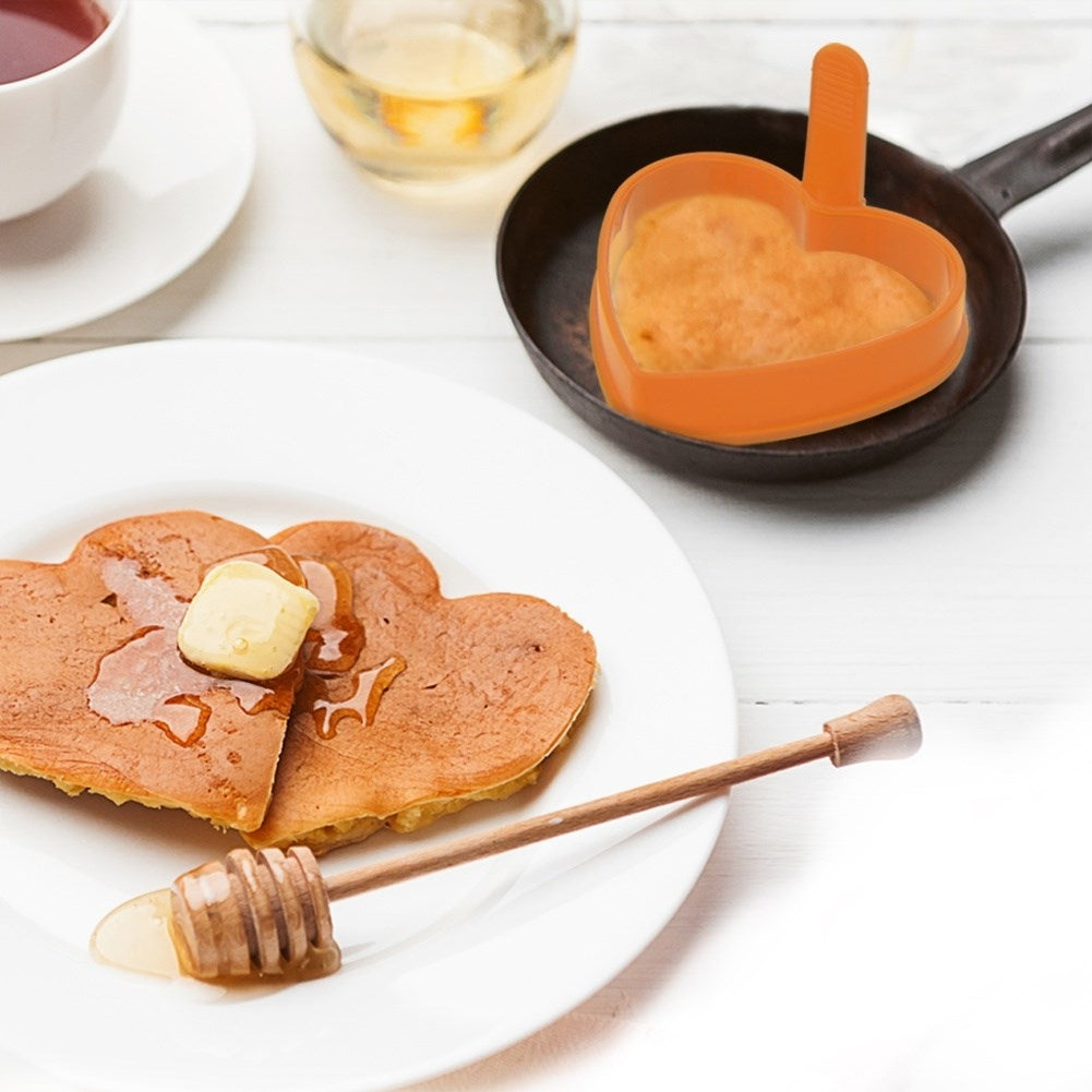 Tortitas en forma de corazón con mantequilla y miel en un plato, cerca un dosificador de miel.