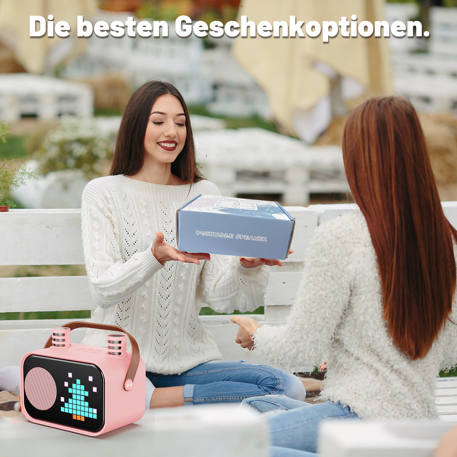 Zwei Frauen sitzen draußen. Eine gibt der anderen eine Geschenkbox.