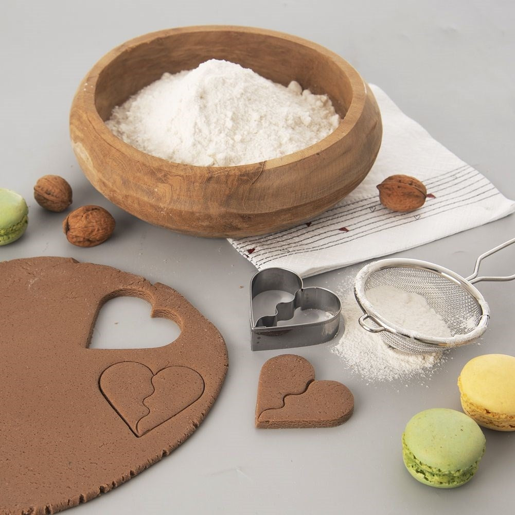 Masa marrón con cortador de corazón, harina en cuenco de madera, nueces, macarons.