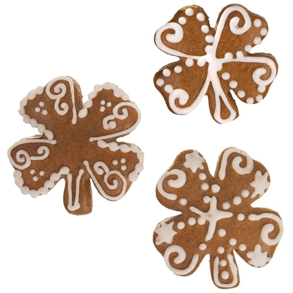 Tres galletas de jengibre marrones en forma de trébol decoradas con glaseado blanco.