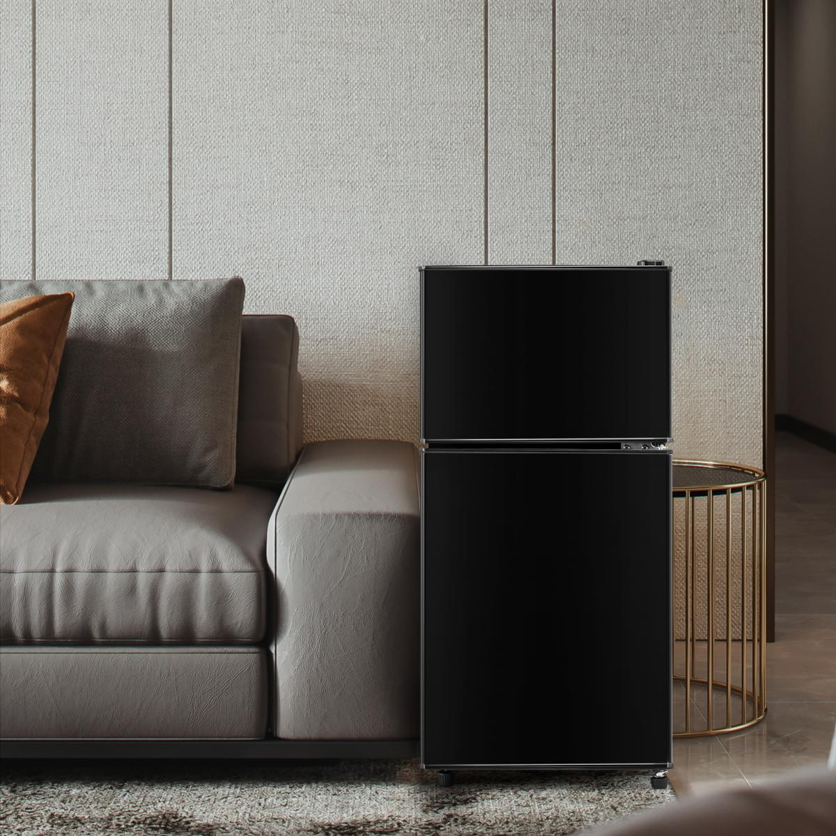 Ein schwarzer Kühlschrank steht neben einem grauen Sofa mit braunen Kissen.